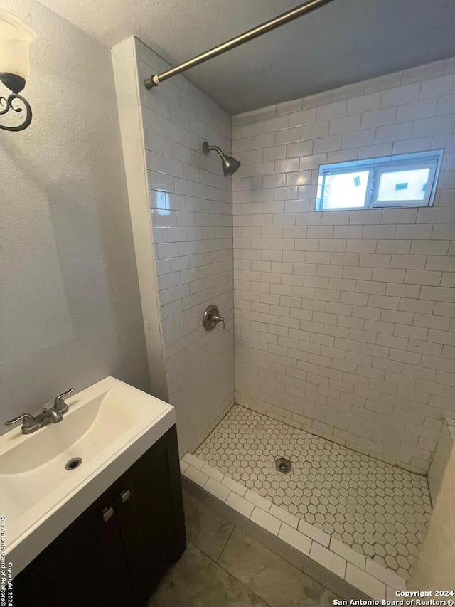 bathroom featuring tile floors, a tile shower, and vanity