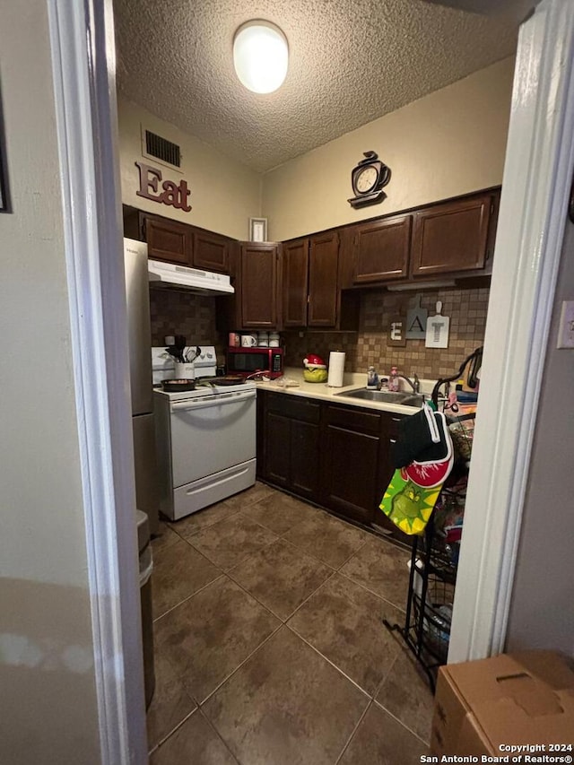 kitchen with white range with gas stovetop, dark brown cabinets, a textured ceiling, backsplash, and dark tile flooring