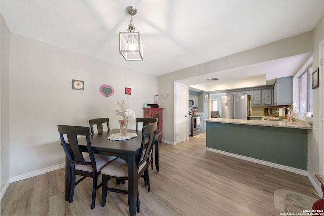 dining area featuring a notable chandelier, sink, and light wood-type flooring