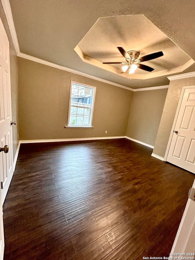 unfurnished bedroom featuring ceiling fan, a textured ceiling, ornamental molding, dark wood-type flooring, and a raised ceiling