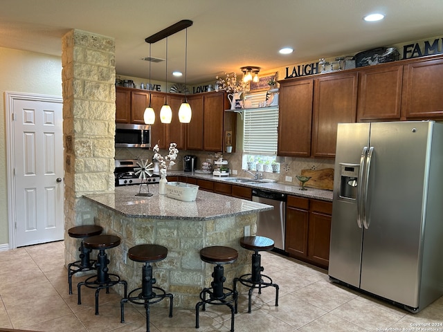 kitchen featuring dark stone counters, hanging light fixtures, stainless steel appliances, light tile flooring, and a kitchen bar