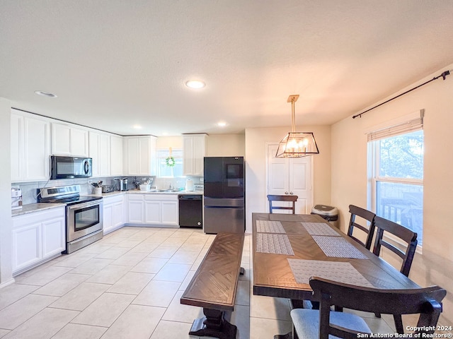 kitchen featuring light tile floors, hanging light fixtures, black appliances, a notable chandelier, and white cabinetry