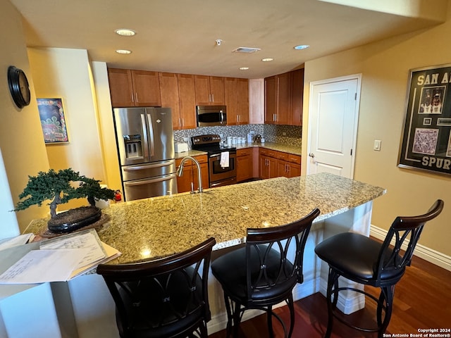 kitchen with backsplash, dark wood-type flooring, a kitchen bar, stainless steel appliances, and light stone counters