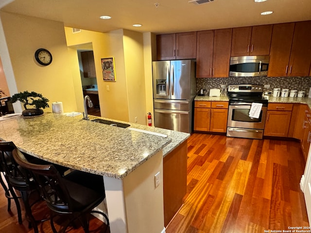 kitchen featuring a breakfast bar area, stainless steel appliances, backsplash, dark hardwood / wood-style flooring, and light stone countertops