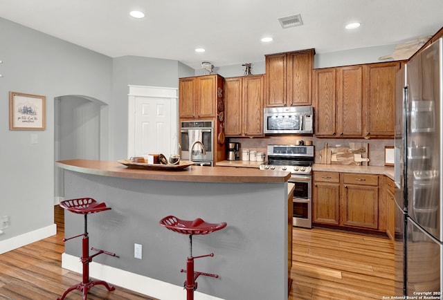 kitchen featuring light hardwood / wood-style flooring, a kitchen bar, tasteful backsplash, and stainless steel appliances