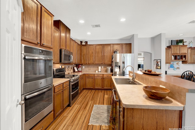 kitchen featuring appliances with stainless steel finishes, tasteful backsplash, sink, light hardwood / wood-style flooring, and a center island with sink