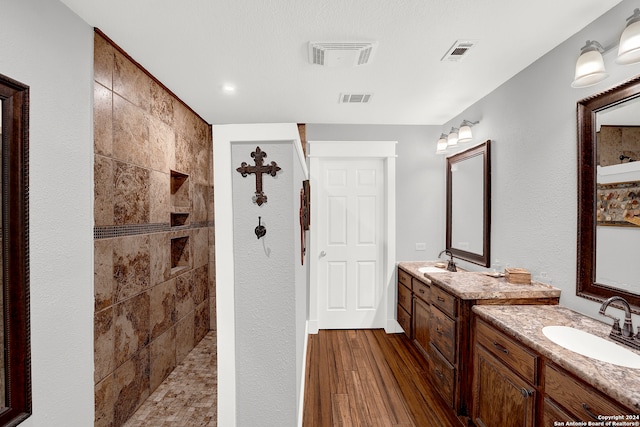 bathroom with tiled shower, double vanity, and wood-type flooring