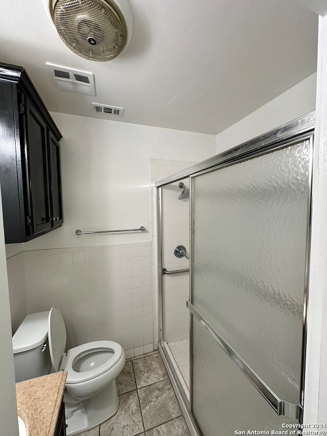 bathroom with toilet, vanity, a shower with door, tile walls, and tile floors