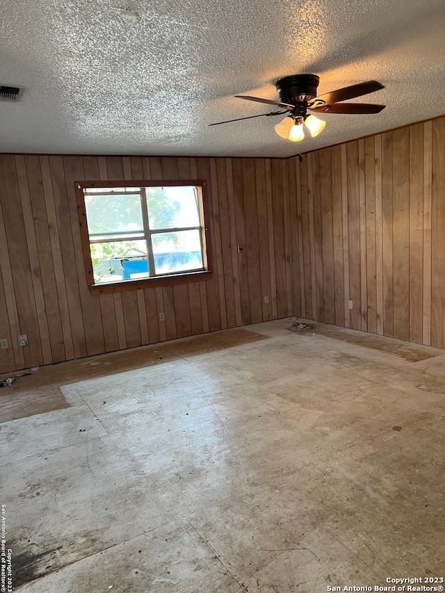 spare room featuring wood walls, a textured ceiling, and ceiling fan