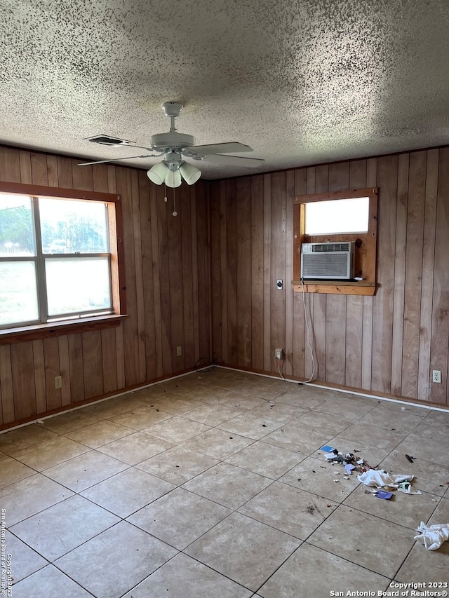 spare room featuring light tile flooring, a textured ceiling, wooden walls, and ceiling fan