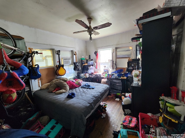 bedroom with a wall mounted air conditioner, wood-type flooring, and ceiling fan