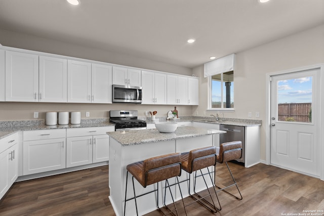 kitchen featuring light stone countertops, stainless steel appliances, white cabinets, a center island, and dark hardwood / wood-style flooring