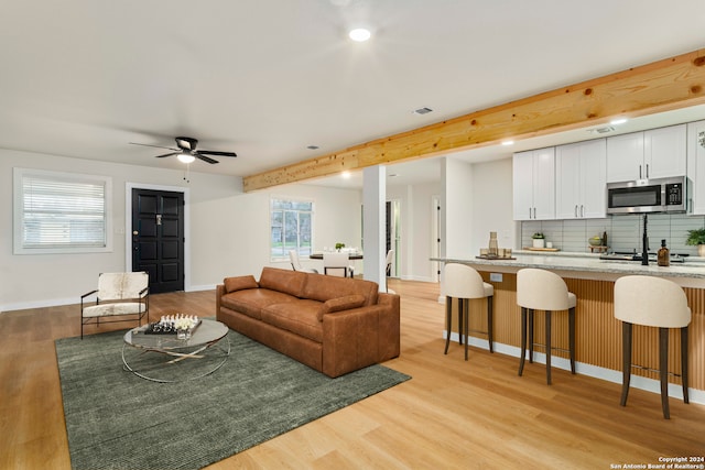 living room with ceiling fan, beam ceiling, and light hardwood / wood-style floors