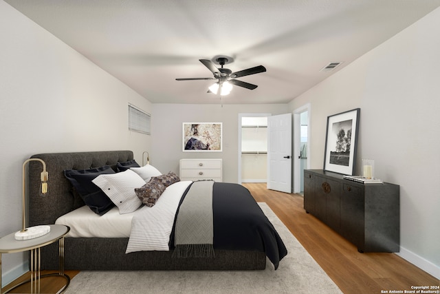 bedroom featuring a walk in closet, a closet, ceiling fan, and light wood-type flooring