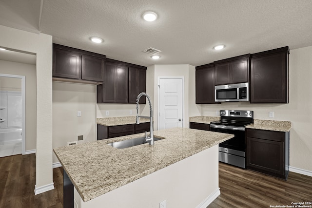 kitchen featuring stainless steel appliances, a textured ceiling, a center island with sink, dark hardwood / wood-style floors, and sink