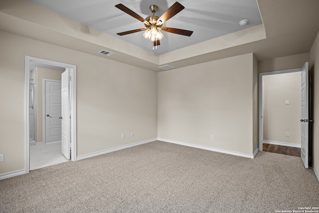 unfurnished bedroom with light carpet, a tray ceiling, connected bathroom, and ceiling fan