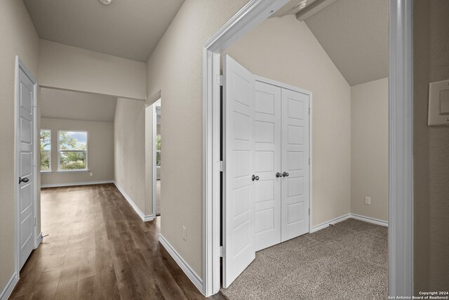 corridor with wood-type flooring and vaulted ceiling with beams