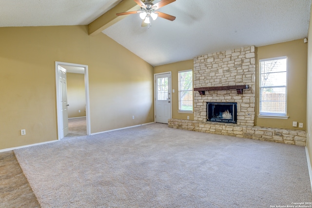 unfurnished living room with light colored carpet, ceiling fan, a fireplace, beam ceiling, and a textured ceiling