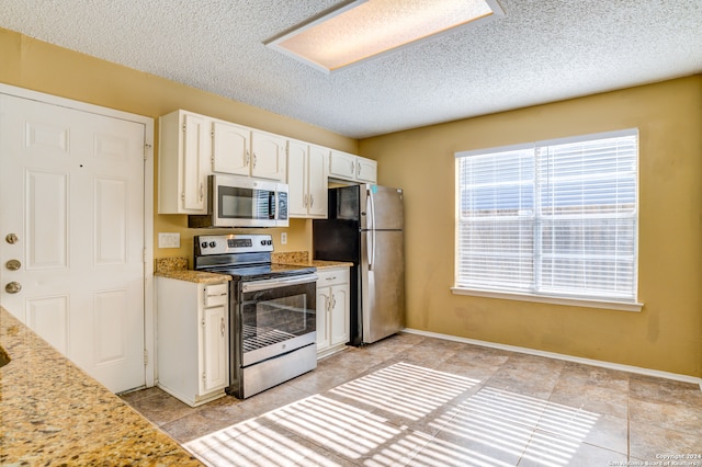 kitchen featuring white cabinets, appliances with stainless steel finishes, light stone counters, and light tile floors