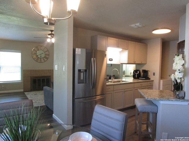 kitchen with dark wood-type flooring, sink, light stone countertops, ceiling fan, and stainless steel refrigerator with ice dispenser