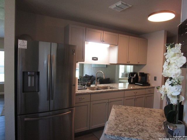 kitchen featuring stainless steel refrigerator with ice dispenser, light stone counters, and sink