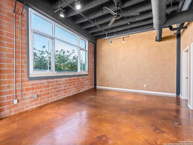 unfurnished room with brick wall, track lighting, ceiling fan, and concrete flooring