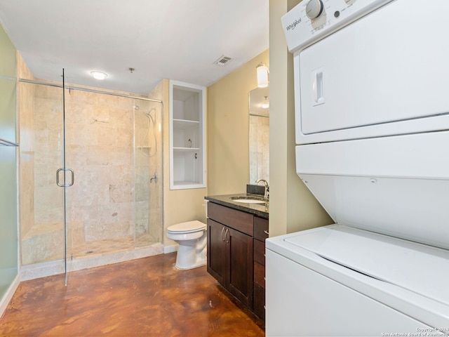 bathroom with concrete flooring, stacked washing maching and dryer, a shower with shower door, toilet, and vanity