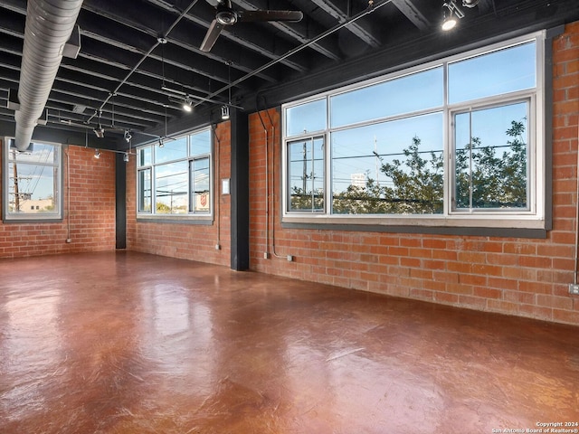 basement featuring a healthy amount of sunlight, brick wall, and track lighting