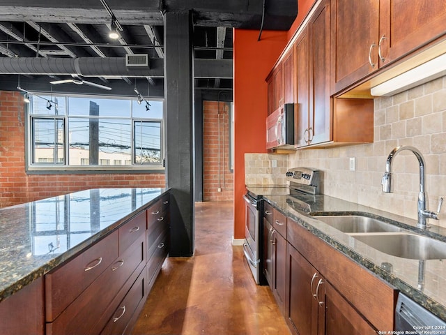 kitchen with brick wall, dark stone counters, stainless steel appliances, backsplash, and sink