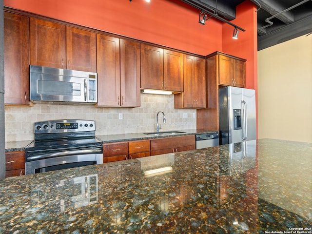 kitchen with sink, tasteful backsplash, dark stone countertops, and stainless steel appliances