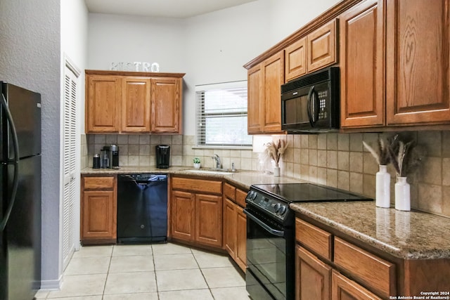 kitchen with tasteful backsplash, light tile flooring, black appliances, dark stone countertops, and sink