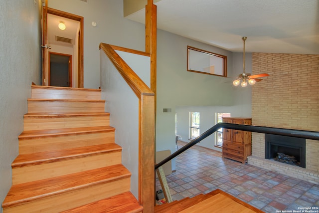 stairs with tile floors, ceiling fan, a fireplace, and lofted ceiling