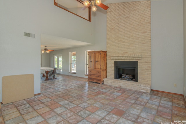 unfurnished living room featuring brick wall, a towering ceiling, a fireplace, ceiling fan, and tile floors