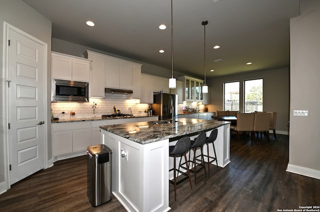 kitchen featuring appliances with stainless steel finishes, decorative light fixtures, a kitchen breakfast bar, dark hardwood / wood-style flooring, and a kitchen island with sink