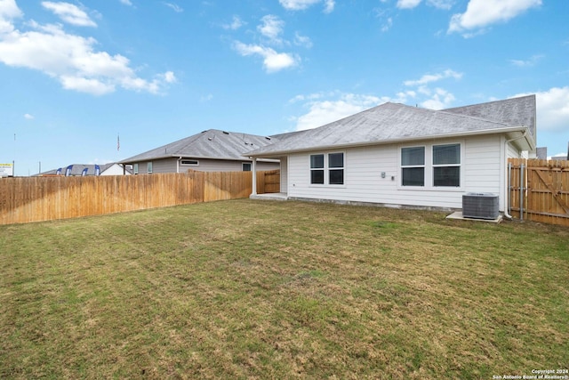 rear view of house with central AC unit and a lawn