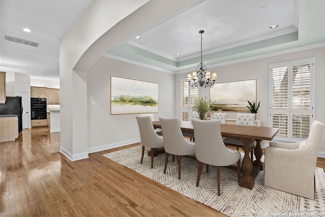 dining room with a chandelier, a raised ceiling, a healthy amount of sunlight, and light wood-type flooring