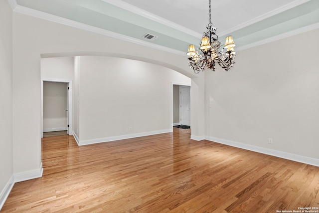 empty room with a chandelier, ornamental molding, and light wood-type flooring