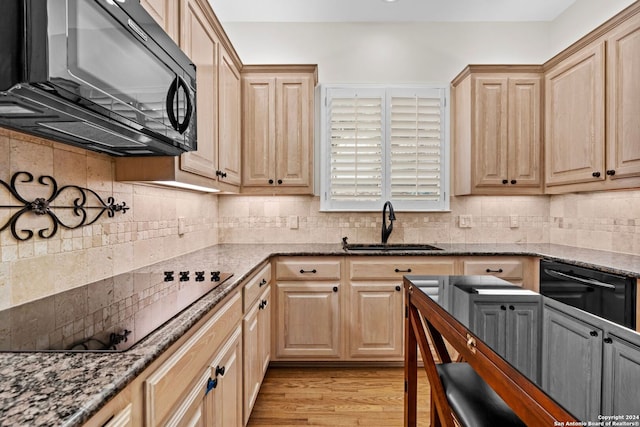 kitchen with backsplash, black appliances, light hardwood / wood-style floors, sink, and dark stone counters