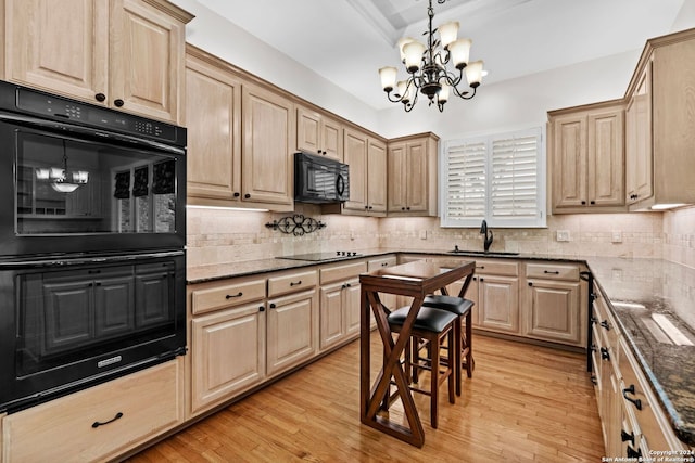 kitchen with dark stone counters, a notable chandelier, light wood-type flooring, black appliances, and sink