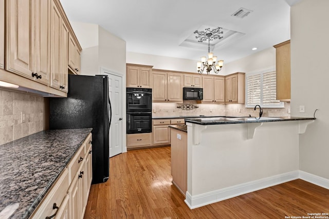 kitchen featuring light wood-type flooring, tasteful backsplash, black appliances, and an inviting chandelier