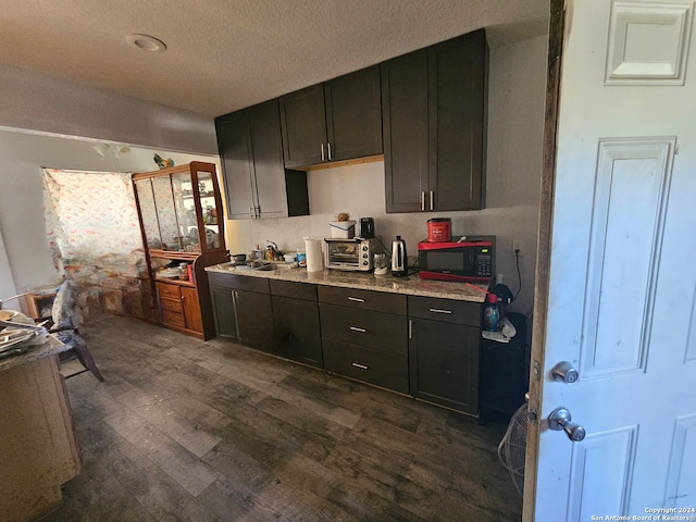 kitchen with sink, light stone counters, dark hardwood / wood-style flooring, a textured ceiling, and dark brown cabinetry