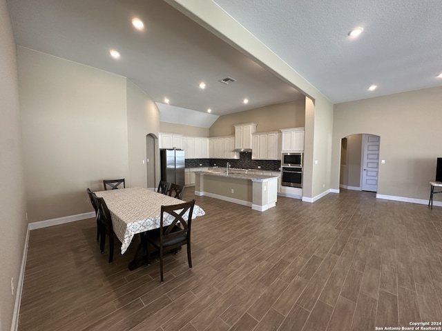 dining space with a textured ceiling, sink, lofted ceiling, and dark wood-type flooring