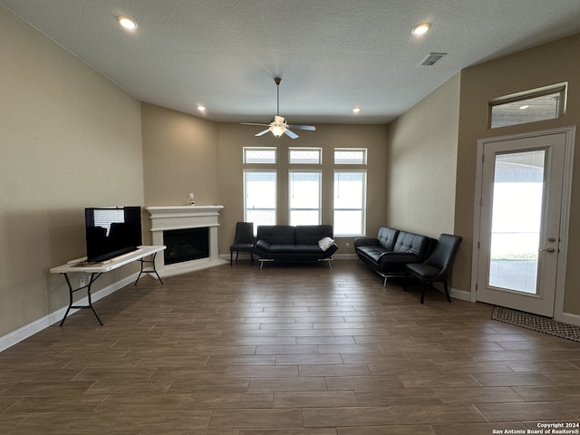 living room with ceiling fan, plenty of natural light, dark hardwood / wood-style floors, and a textured ceiling