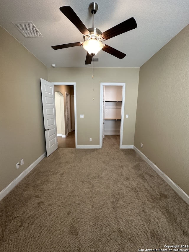 unfurnished bedroom with ceiling fan, a closet, carpet, and a spacious closet