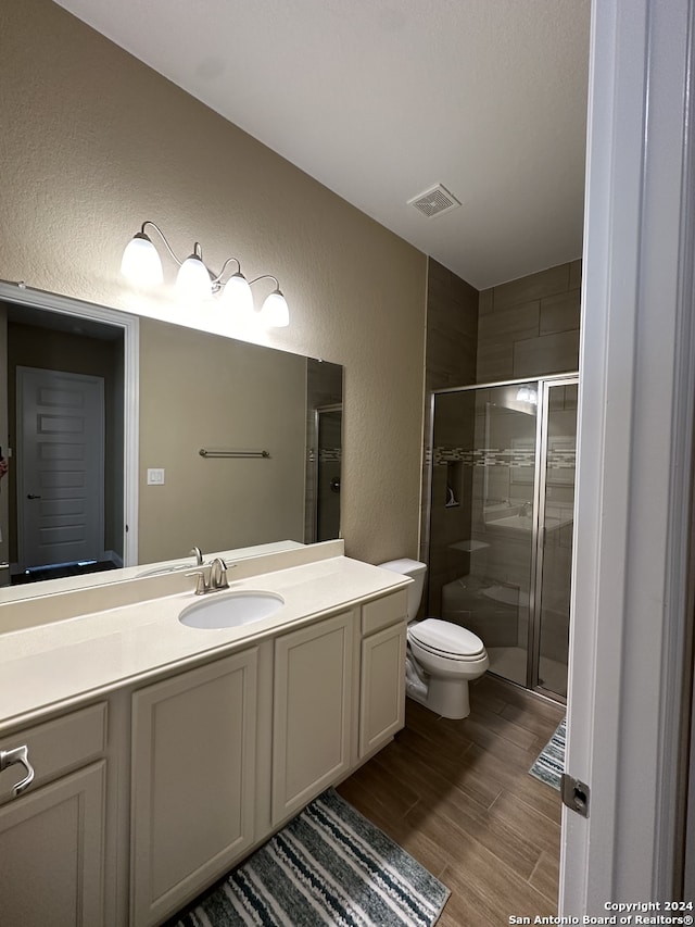 bathroom with an enclosed shower, vanity, toilet, and hardwood / wood-style flooring