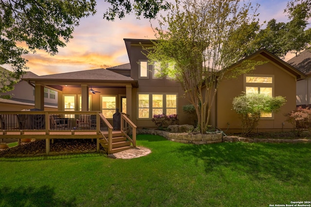 back house at dusk with a deck and a lawn