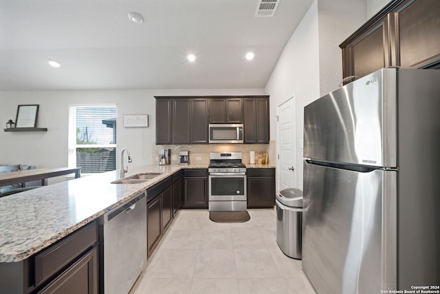 kitchen featuring appliances with stainless steel finishes, light tile flooring, light stone counters, sink, and dark brown cabinets