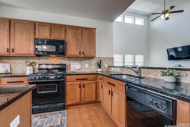 kitchen featuring sink, ceiling fan, dark stone counters, black appliances, and light wood-type flooring