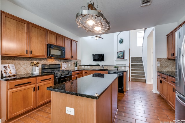 kitchen with black appliances, sink, dark stone countertops, a kitchen island, and tasteful backsplash