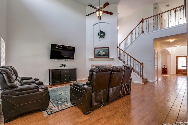 living room with light hardwood / wood-style floors, ceiling fan, and a towering ceiling